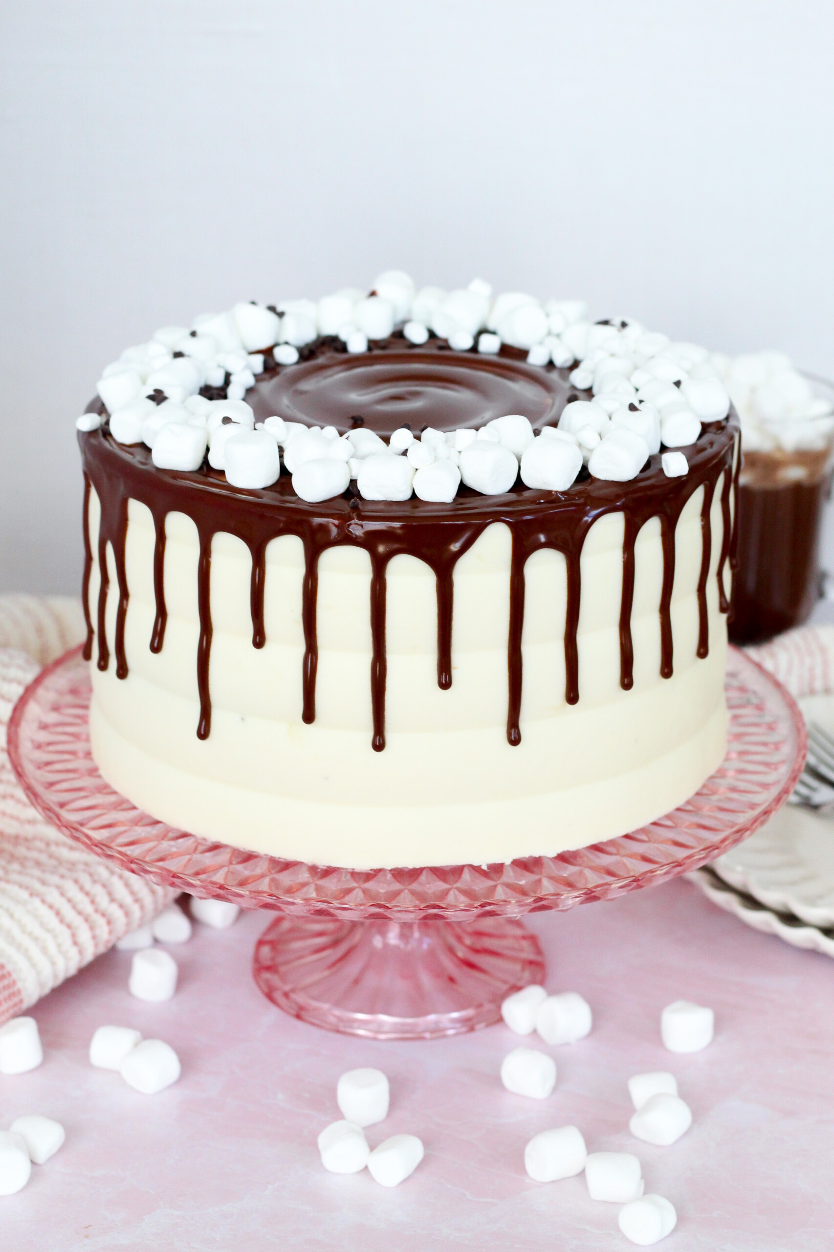 Cake on a cake stand with a chocolate drip and marshmallows on it.