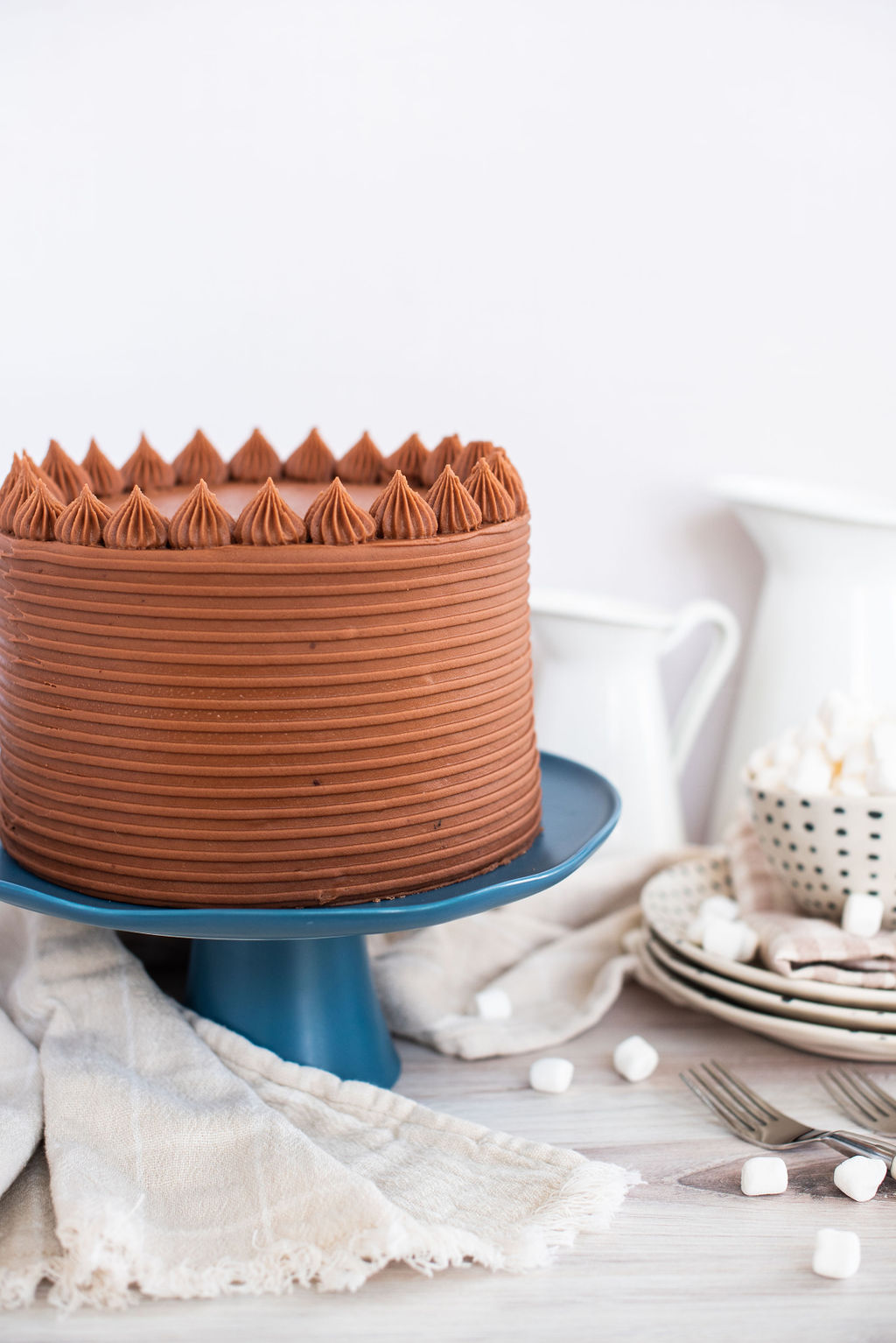 Chocolate cake on a blue cake stand with plates next to it.
